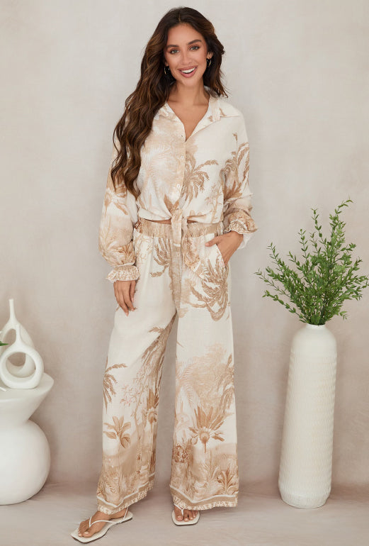 Woman wearing a floral outfit standing against a neutral background with decorative vases.