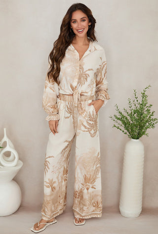 Woman wearing a floral outfit standing against a neutral background with decorative vases.